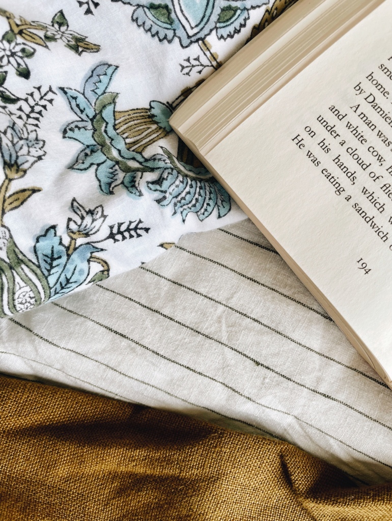 Looking down on an open book surrounded by linen sheets and an Indian cotton block patterned blanket.